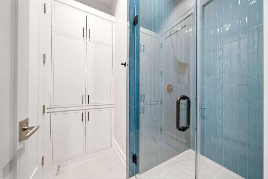 Ensuite bath with bold blue tile shower and plentiful cabinet storage. Ensuite bath with bold blue tile shower and plentiful cabinet storage.