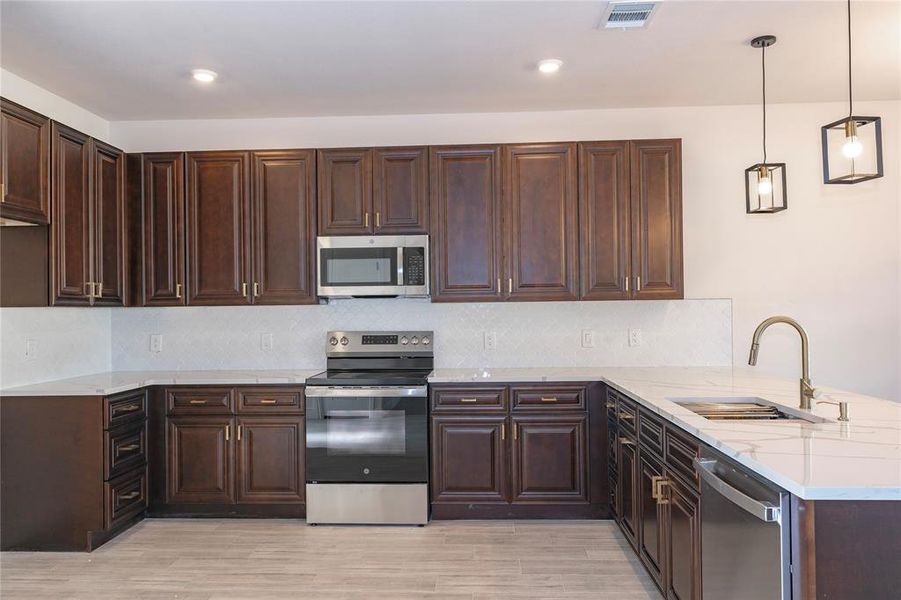 Kitchen featuring appliances with stainless steel finishes, light hardwood / wood-style flooring, sink, and pendant lighting