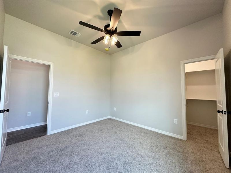 Unfurnished bedroom with a spacious closet, light colored carpet, and ceiling fan Unfurnished bedroom with a spacious closet, light colored carpet, and ceiling fan