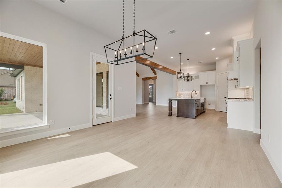 Kitchen featuring open floor plan, a breakfast bar area, a chandelier, a kitchen island with sink, and white cabinets