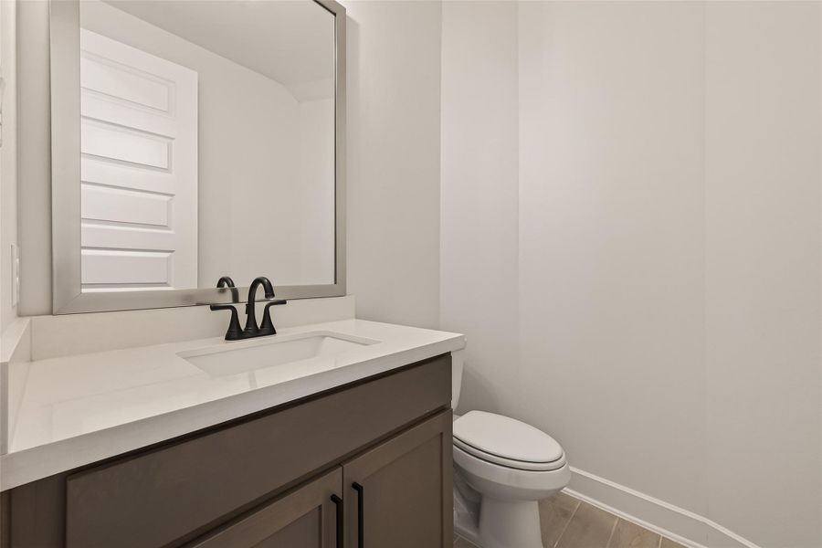This is a modern half-bathroom featuring a sleek vanity with a large mirror, dark cabinetry, and a white countertop. The minimalist design offers a clean and fresh look.