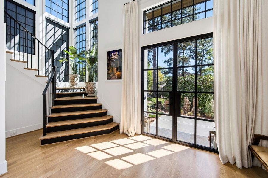 Light-filled entry with soaring ceilings, dramatic steel-framed doors, and a statement staircase with modern railing. Floor-to-ceiling windows bring in natural light and create a seamless indoor-outdoor connection.
