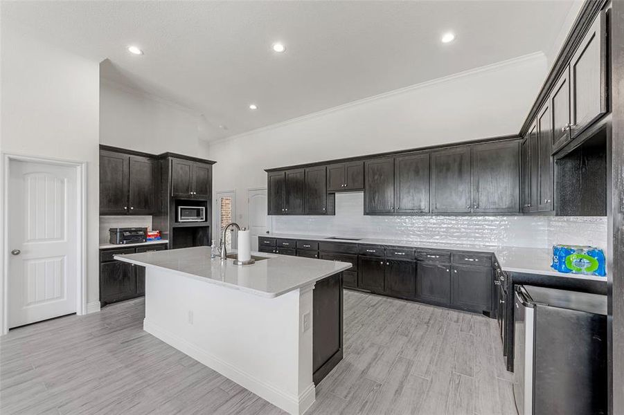 Kitchen with stainless steel microwave, a sink, crown molding, backsplash, and a kitchen island with sink