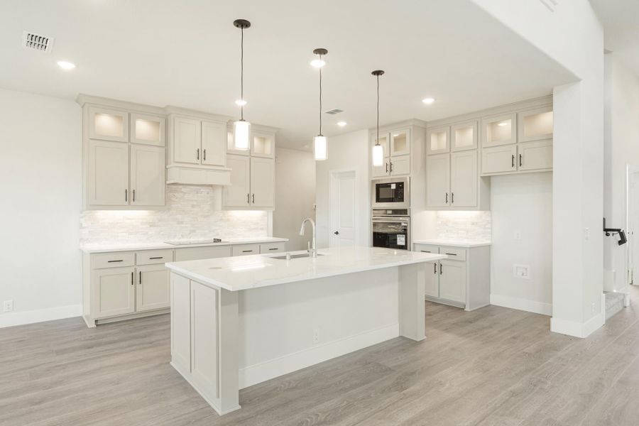 White kitchen with large center island, pendant lights, gray cabinets, and stainless steel appliances on wood floors
