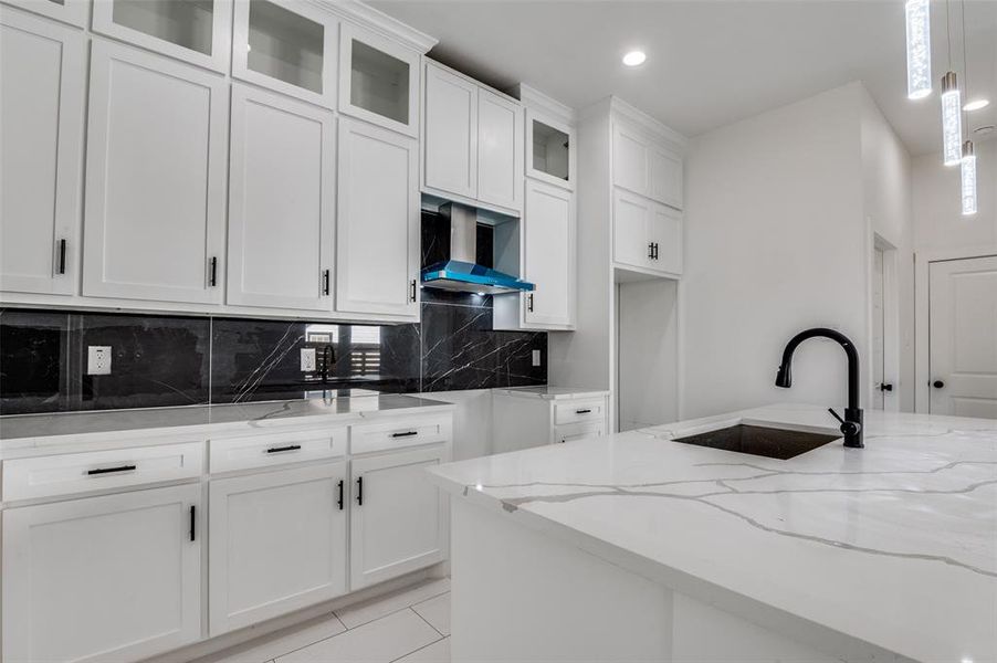 Kitchen with light stone countertops, glass insert cabinets, backsplash, hanging light fixtures, and recessed lighting