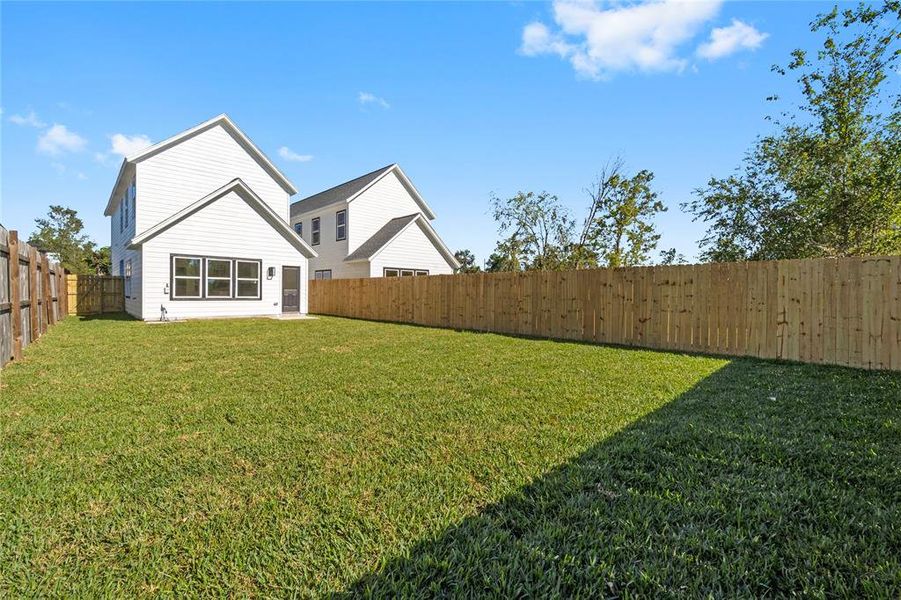 Another angle of the backyard showcases the generous outdoor space and a view of the neighboring new construction, highlighting the modern design throughout. (Photo may be enhanced and may include virtual staging)