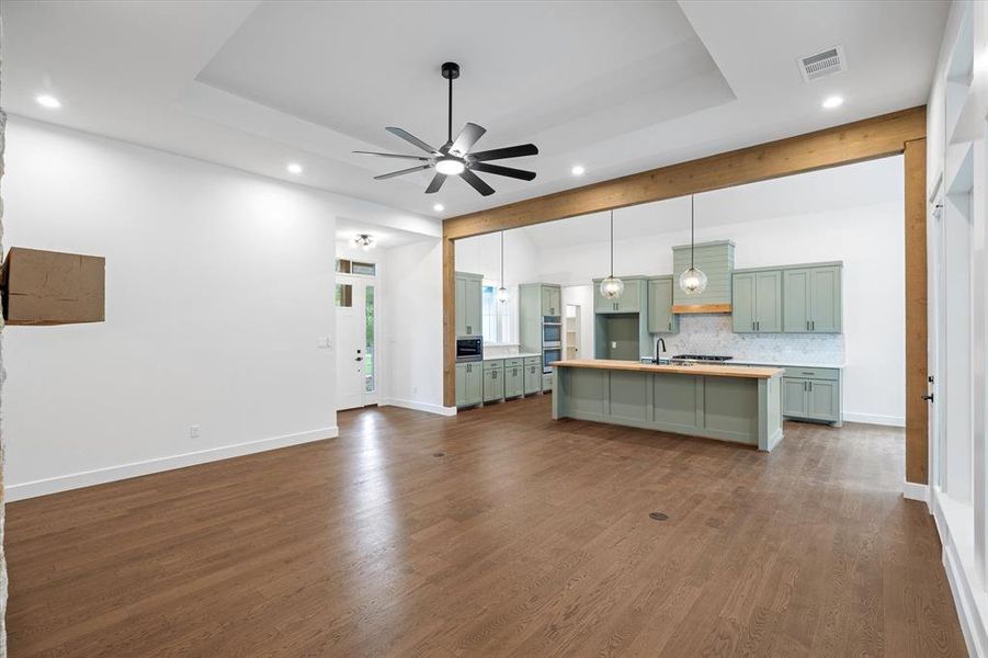 living room featuring dark wood-style floors, recessed lighting, ceiling fan, beamed ceiling, and a tray ceiling living room featuring dark wood-style floors, recessed lighting, ceiling fan, beamed ceiling, and a tray ceiling