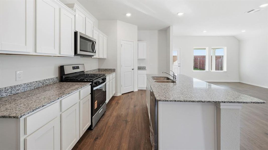 Kitchen featuring stainless steel appliances, light stone counters, white cabinets, dark wood-style flooring, and a kitchen island with sink Kitchen featuring stainless steel appliances, light stone counters, white cabinets, dark wood-style flooring, and a kitchen island with sink