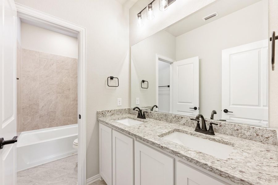 Bathroom with double sink vanity, granite countertops, white cabinets, and tiled tub-shower combo Bathroom with double sink vanity, granite countertops, white cabinets, and tiled tub-shower combo