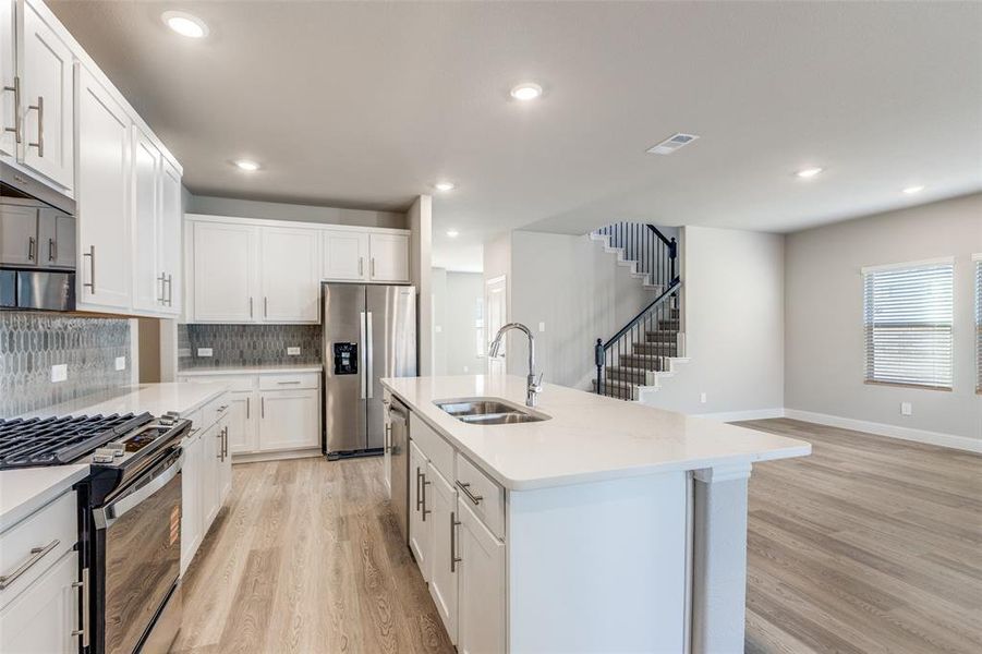 Kitchen with appliances with stainless steel finishes, light wood-type flooring, white cabinets, decorative backsplash, and a center island with sink Kitchen with appliances with stainless steel finishes, light wood-type flooring, white cabinets, decorative backsplash, and a center island with sink