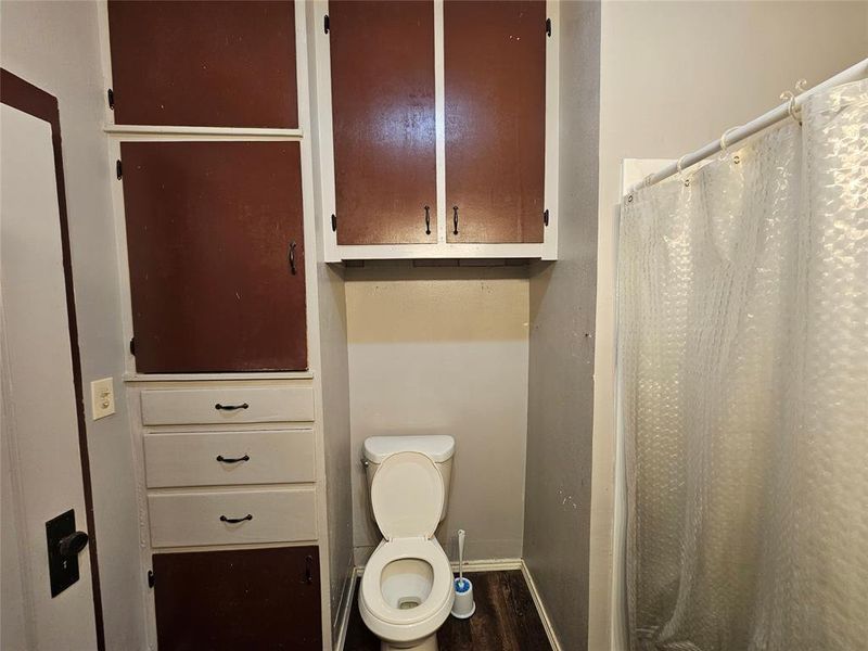 Bathroom with toilet, a shower with shower curtain, and hardwood / wood-style flooring Bathroom with toilet, a shower with shower curtain, and hardwood / wood-style flooring
