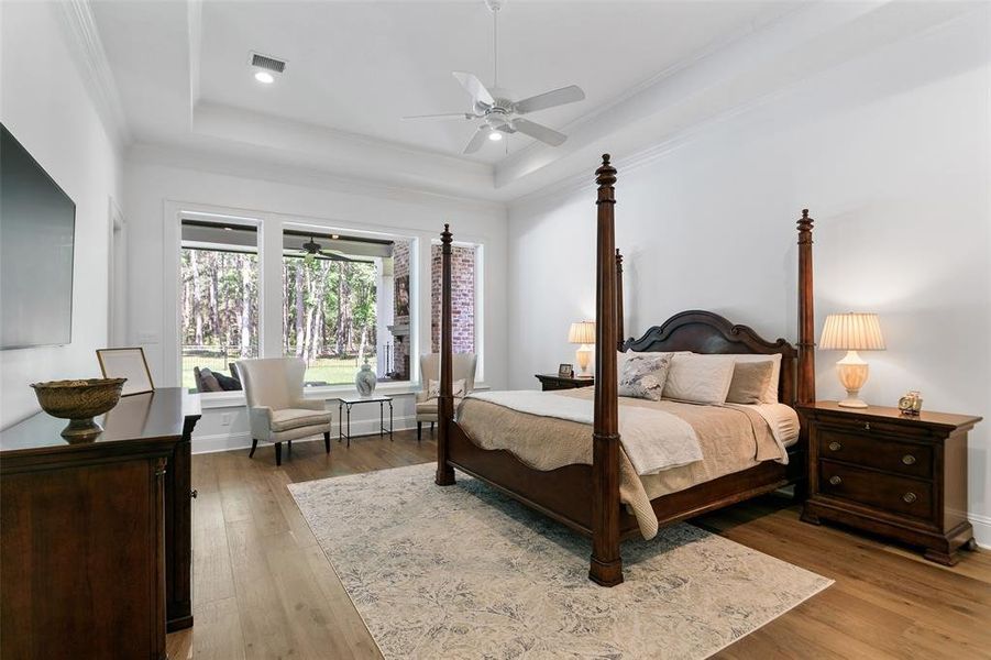 Primary bedroom with wood floors, tray ceiling, crown molding, a private door to the patio, and windows that overlook the covered patio.