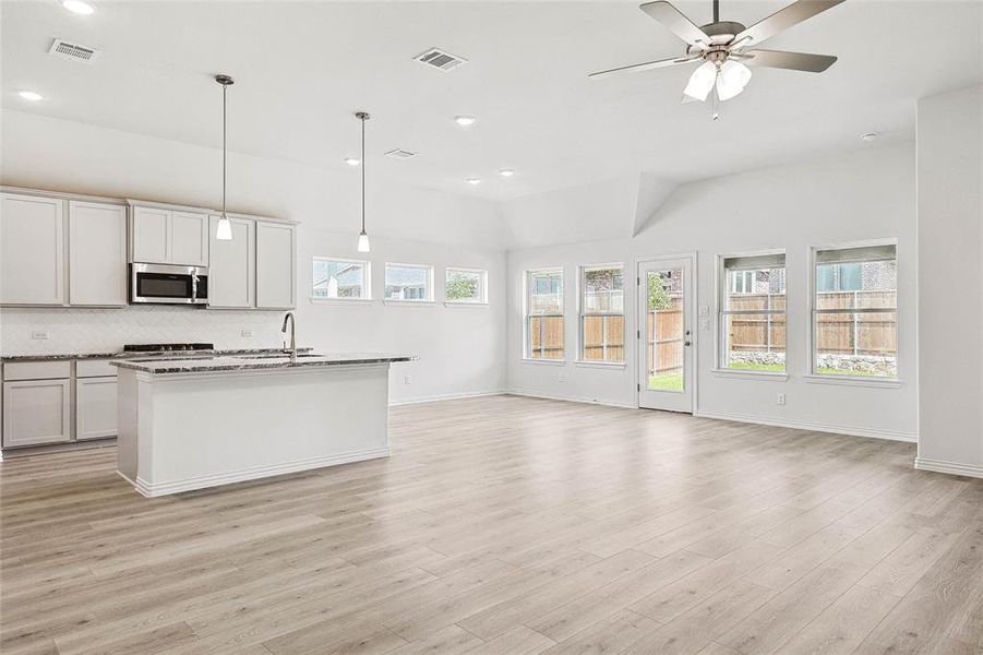 Kitchen featuring light wood-type flooring, pendant lighting, a kitchen island with sink, ceiling fan, and decorative backsplash