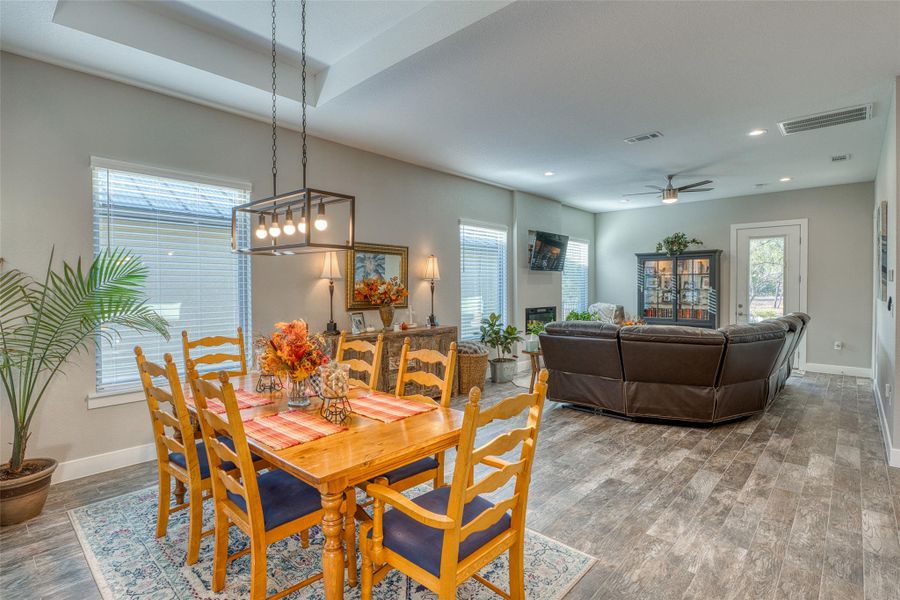 Dining room featuring wood finished floors, ceiling fan, a tray ceiling, recessed lighting, and a glass covered fireplace