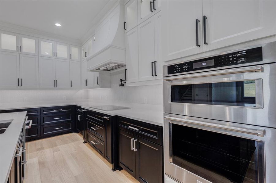 Gourmet kitchen featuring a built-in stainless steel double oven, sleek cooktop, contrasting black and white cabinetry, recessed lighting, and wood-finish flooring