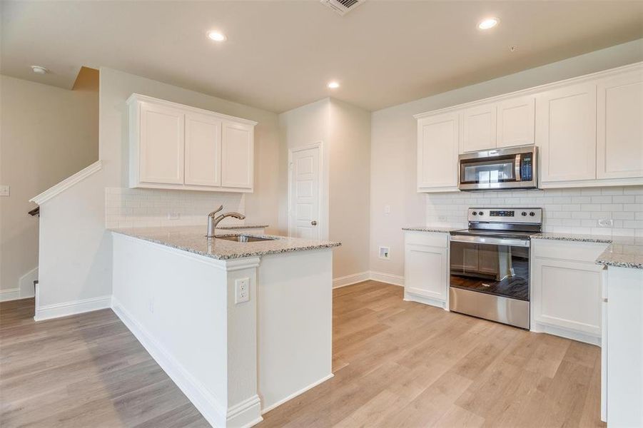 Kitchen featuring light stone counters, stainless steel appliances, white cabinets, and light wood-type flooring