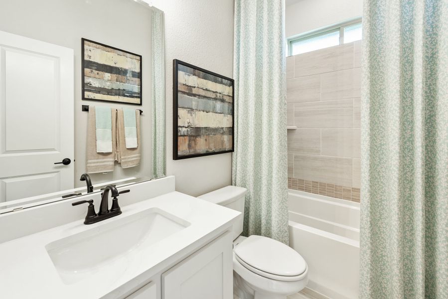 Full bathroom with white vanity, dark faucet, toilet, and tiled tub-shower with curtain
