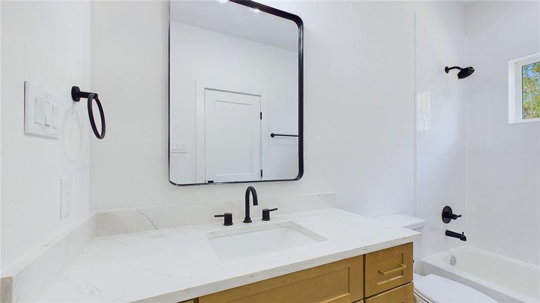 This stylish shared bath showcases elegant finishes throughout. A spacious vanity with an under-mount sink and added storage is topped with white quartz and accented by dark hardware, while the tub and shower combo is framed by classic white subway tiles, creating a clean and timeless look.