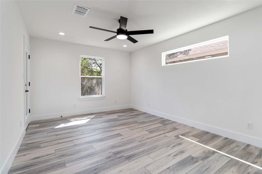 Primary bedroom on the main level highlighted by a ceiling fan, recessed downlights, and a fixed transom window above the bed area. Primary bedroom on the main level highlighted by a ceiling fan, recessed downlights, and a fixed transom window above the bed area.