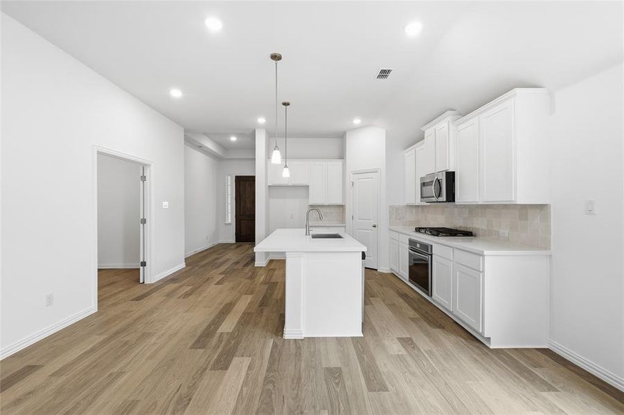 Kitchen featuring an island with pendant lighting, white cabinetry, integrated stainless steel appliances, a tile backsplash, and light wood-finish flooring