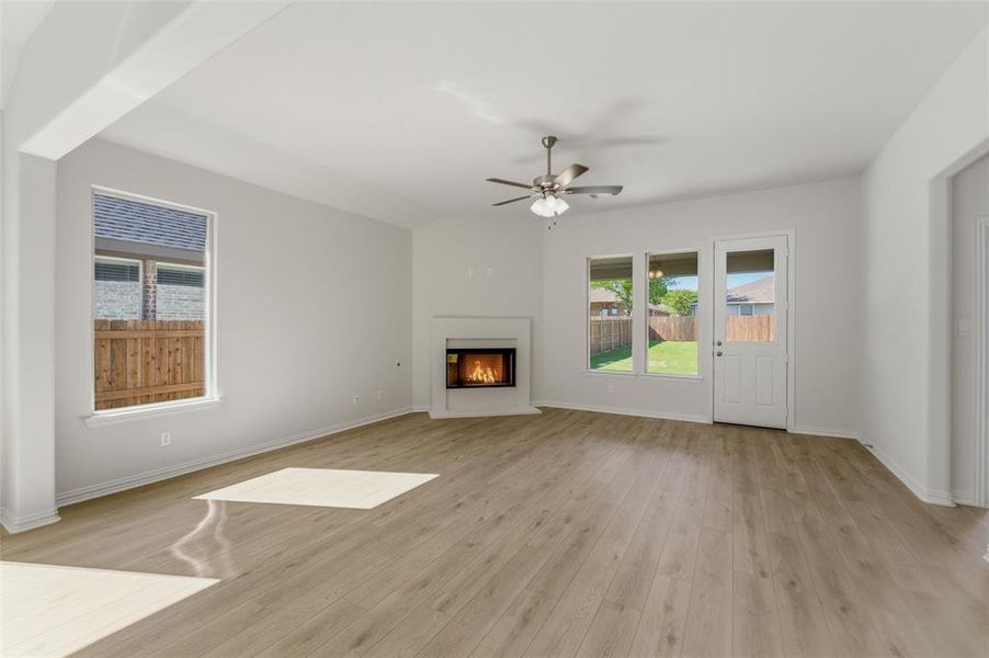 Unfurnished living room with a glass covered fireplace, ceiling fan, light wood-style flooring, and healthy amount of natural light