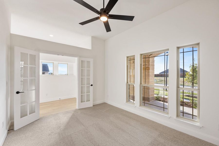 Empty bedroom with carpet, ceiling fan, large windows, and French doors leading to adjacent room Empty bedroom with carpet, ceiling fan, large windows, and French doors leading to adjacent room
