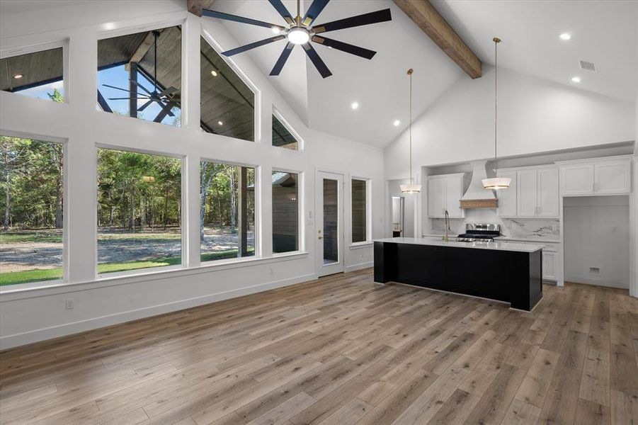 Kitchen with dark cabinetry, high vaulted ceiling, hanging light fixtures, white cabinetry, and a center island with sink