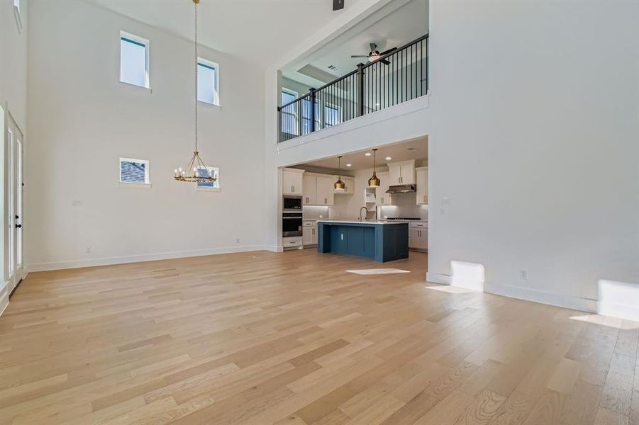 Unfurnished living room with light wood-type flooring, a towering ceiling, a ceiling fan, and a chandelier