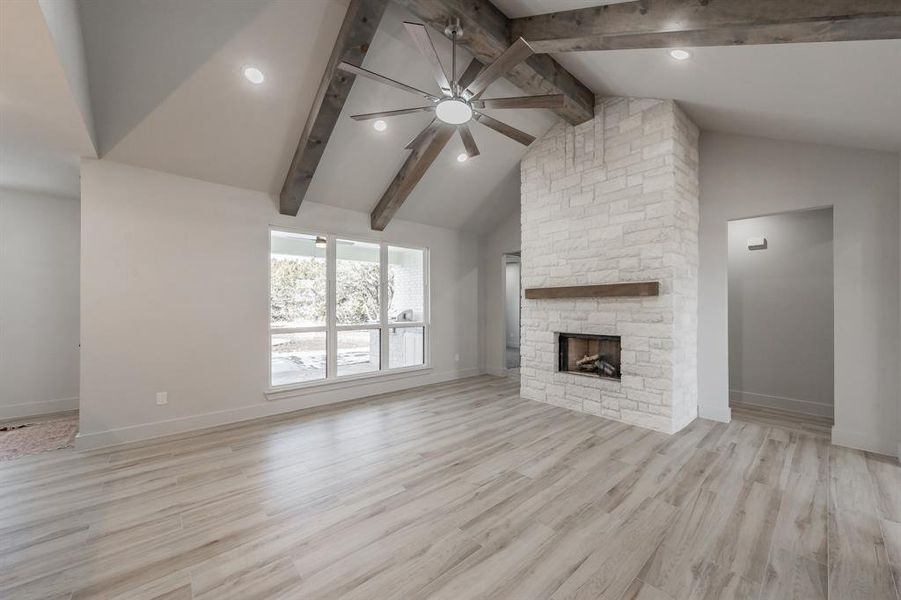Unfurnished living room featuring a ceiling fan, high vaulted ceiling, a fireplace, light wood-type flooring, and beam ceiling