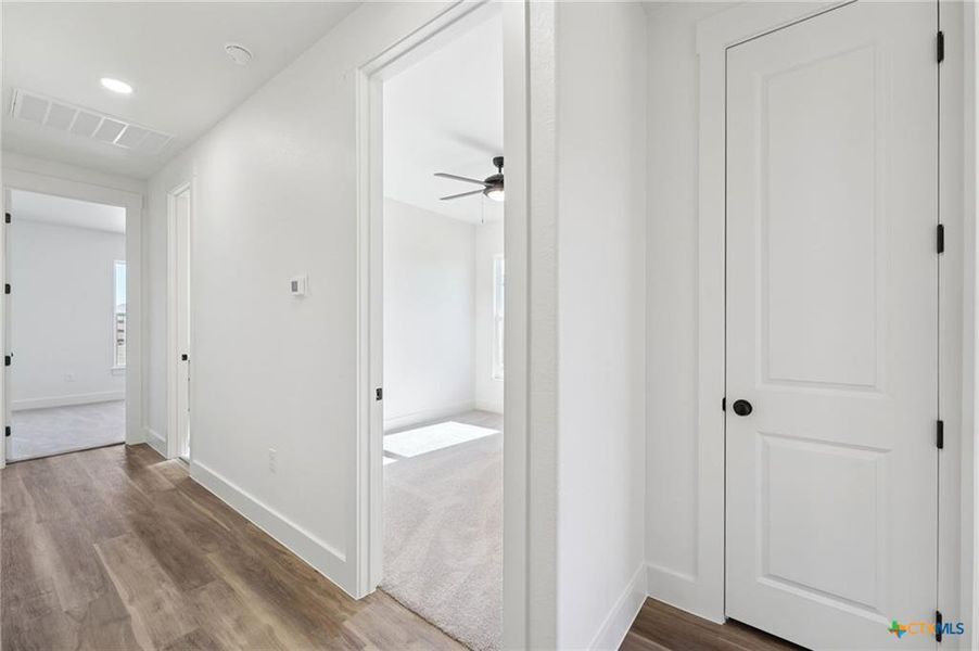 A well-lit corridor with warm wood-look flooring leads to inviting carpeted rooms. A well-lit corridor with warm wood-look flooring leads to inviting carpeted rooms.
