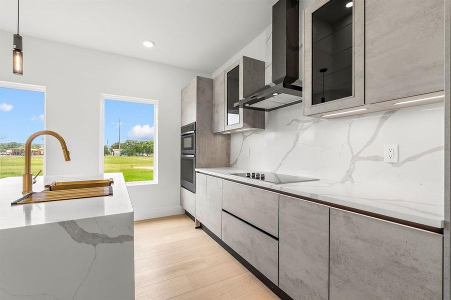 Kitchen with light wood finished floors, backsplash, a sink, wall chimney exhaust hood, and black electric stovetop