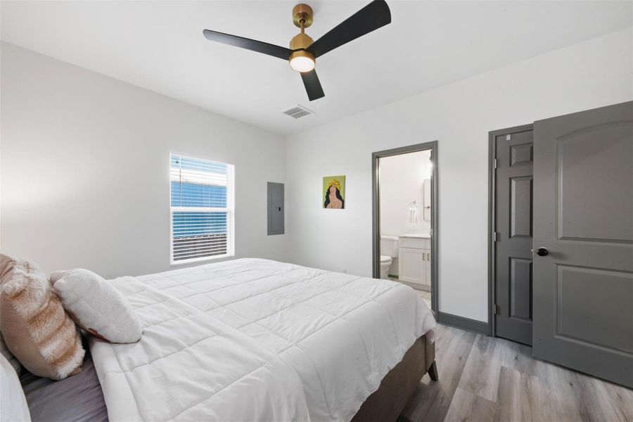 Cozy bedroom with modern ceiling fan, ample natural light from a window, and an ensuite bathroom. Stylish gray doors and light wood flooring enhance the contemporary feel.