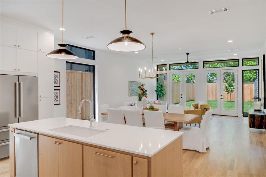 Kitchen with light wood-type flooring, stainless steel appliances, light brown cabinets, sink, and a center island with sink