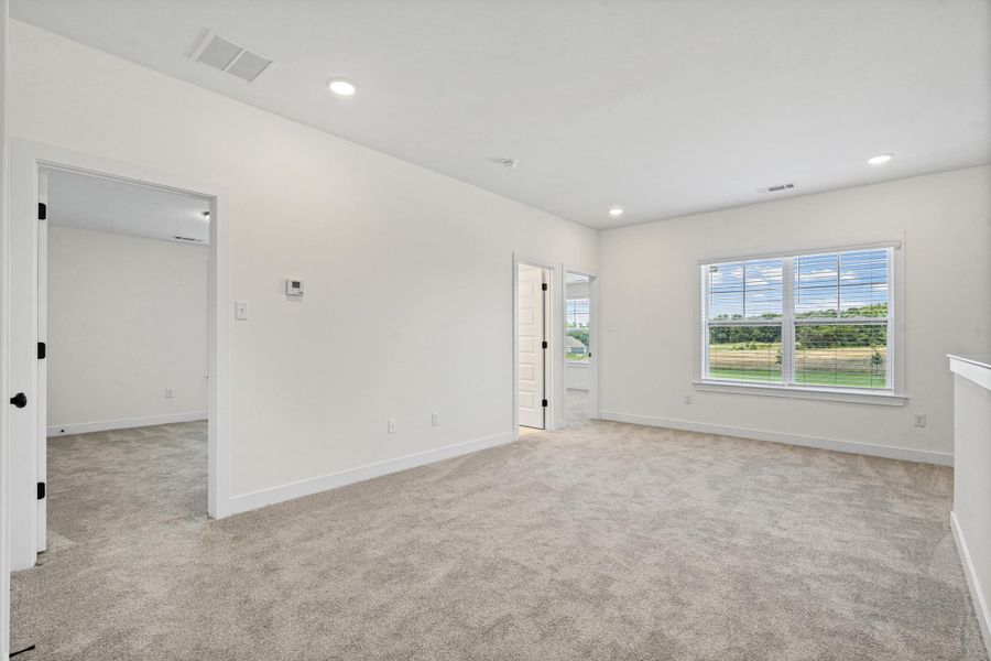 Spacious room featuring light gray carpet flooring, recessed ceiling lighting, and a large window with white blinds Spacious room featuring light gray carpet flooring, recessed ceiling lighting, and a large window with white blinds