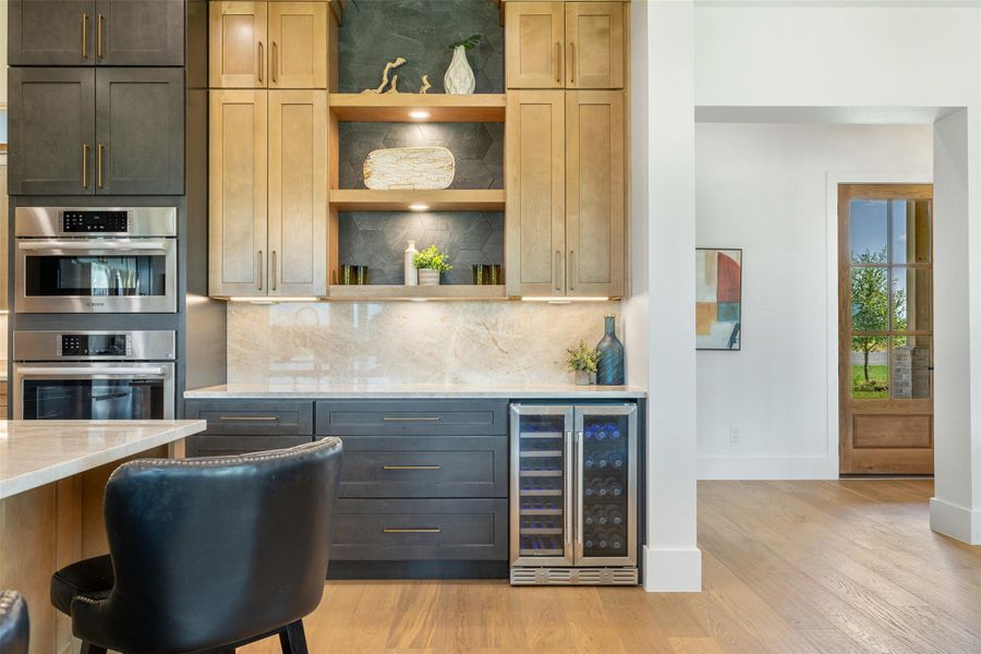 Bar with backsplash, open shelves, wine cooler, light stone counters, and built in oven and convection microwave
