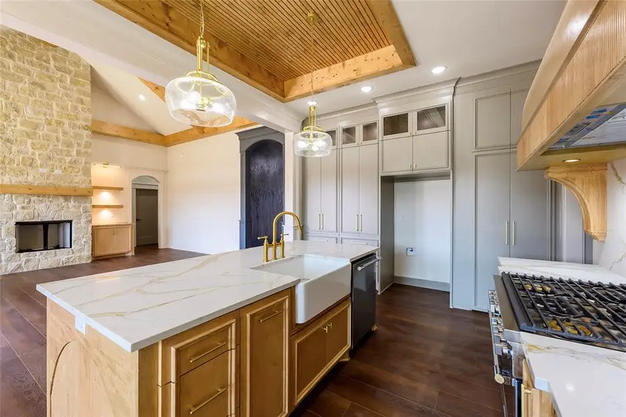 Two tone kitchen featuring hanging light fixtures, gas range, dark wood finished floors, light stone counters, and open floor plan Two tone kitchen featuring hanging light fixtures, gas range, dark wood finished floors, light stone counters, and open floor plan