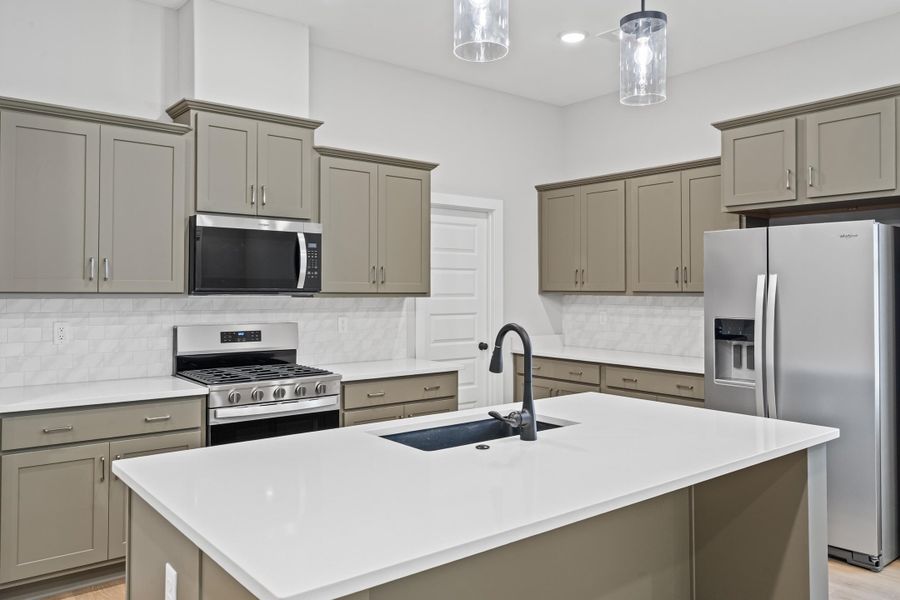 Kitchen featuring appliances with stainless steel finishes, gray cabinets, backsplash, a center island with sink, and light stone counters