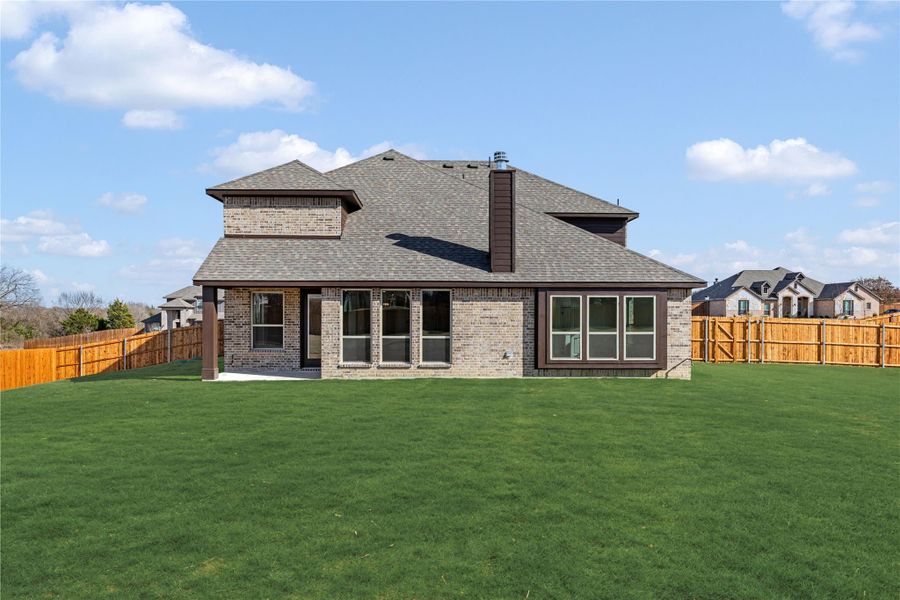 Rear view of two-story brick home with large fenced backyard and green lawn Rear view of two-story brick home with large fenced backyard and green lawn