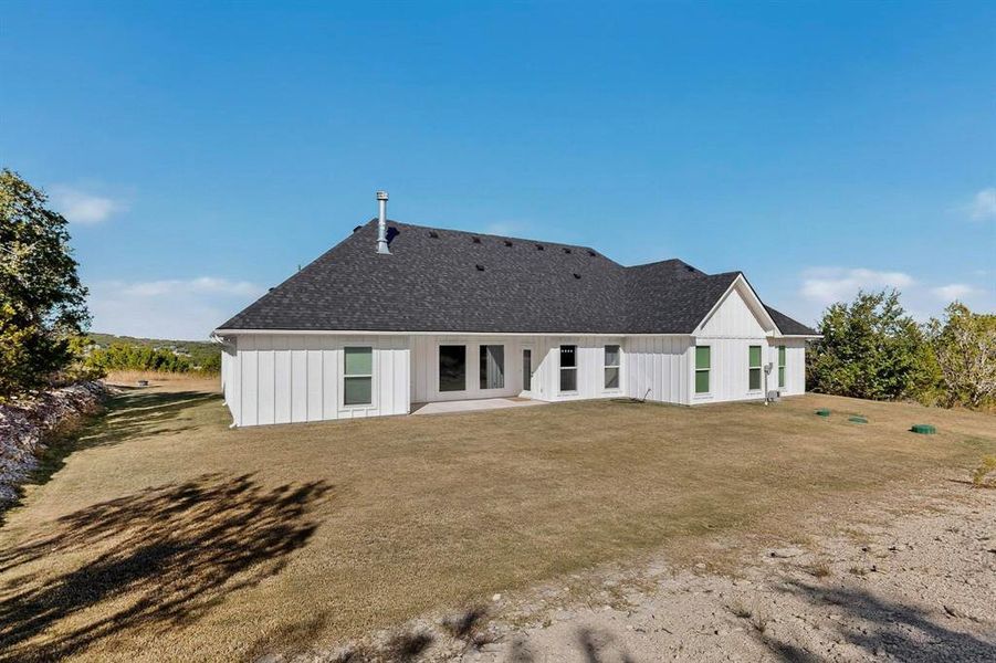 Back of property featuring a patio area, a shingled roof, and a yard