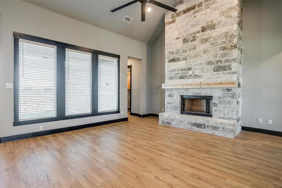 Unfurnished living room with ceiling fan, a fireplace, lofted ceiling, and light wood-type flooring