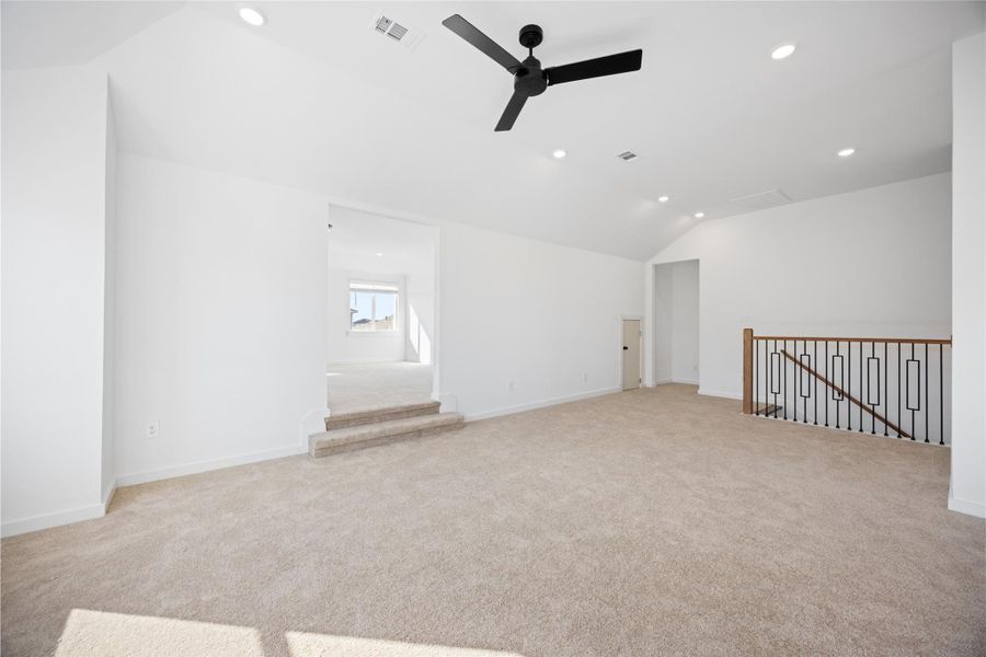 This spacious, carpeted loft features recessed lighting, a modern ceiling fan, and clean white walls. It has an open layout with a railing overlooking a stairwell and leads to a bright area with large windows. This spacious, carpeted loft features recessed lighting, a modern ceiling fan, and clean white walls. It has an open layout with a railing overlooking a stairwell and leads to a bright area with large windows.