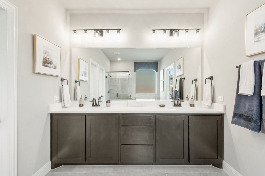 Bathroom with double vanity, dark cabinets, white countertops, and large mirror with overhead lighting Bathroom with double vanity, dark cabinets, white countertops, and large mirror with overhead lighting