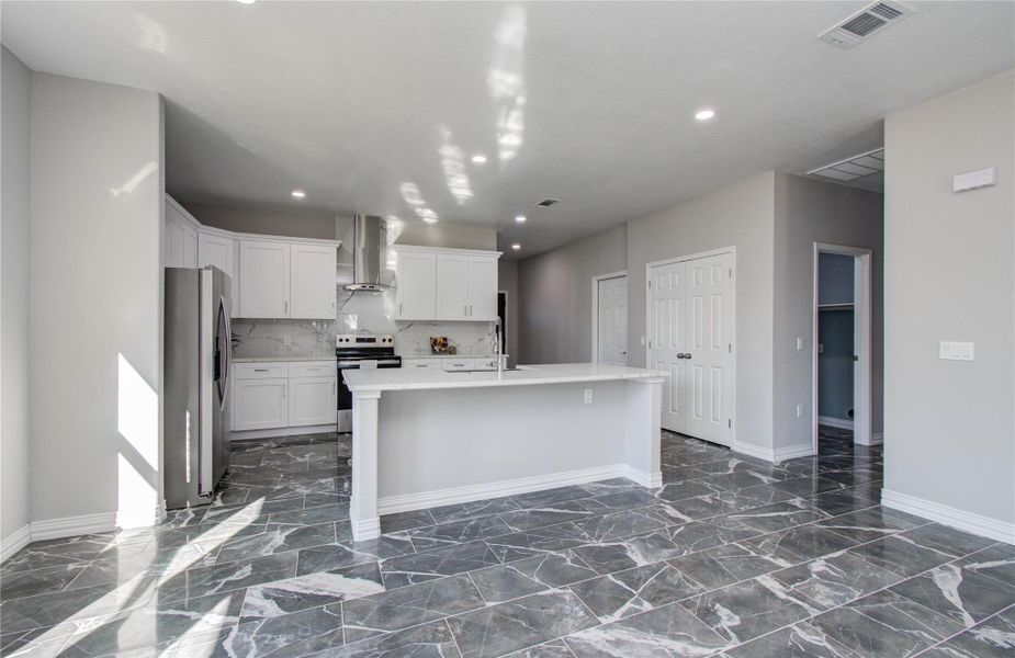 Modern kitchen with sleek gray marble flooring, white cabinetry, and stainless steel appliances. Features an open layout with an island and ample natural light.