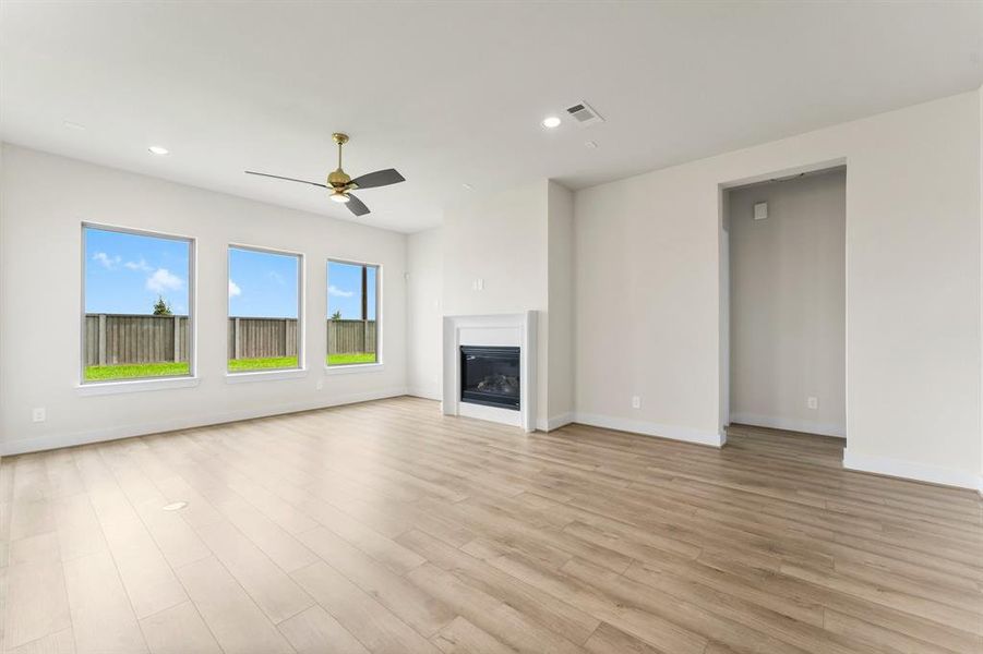 Family Room with Gas Fireplace, Luxury Vinyl Plank Flooring, Fan, and Wall of Windows with Views of the Fenced Back Yard.