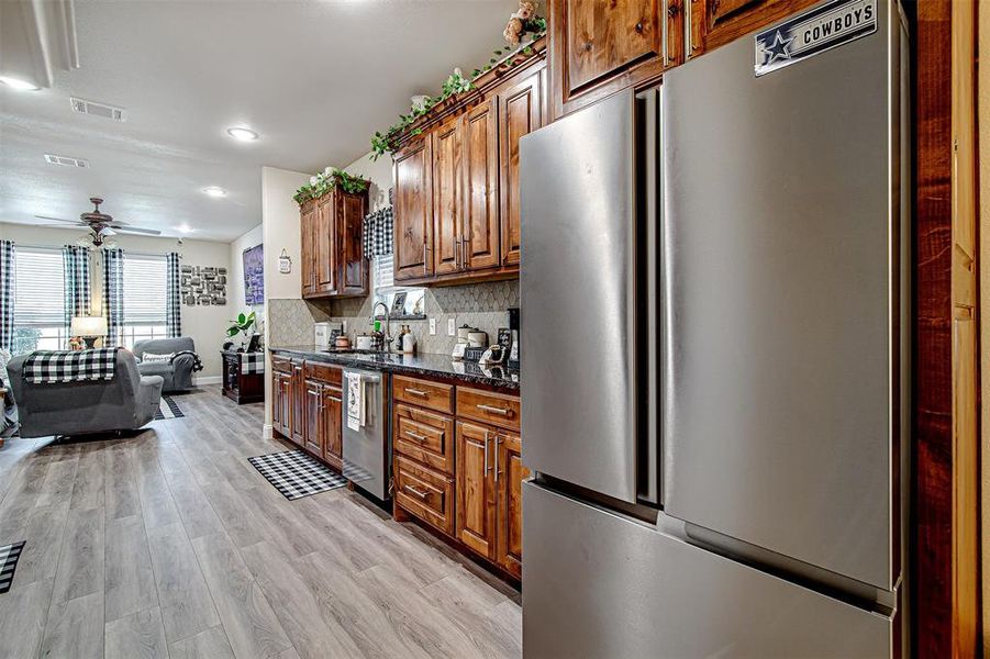 Kitchen with decorative backsplash, dark stone counters, stainless steel appliances, ceiling fan, and light hardwood / wood-style floors