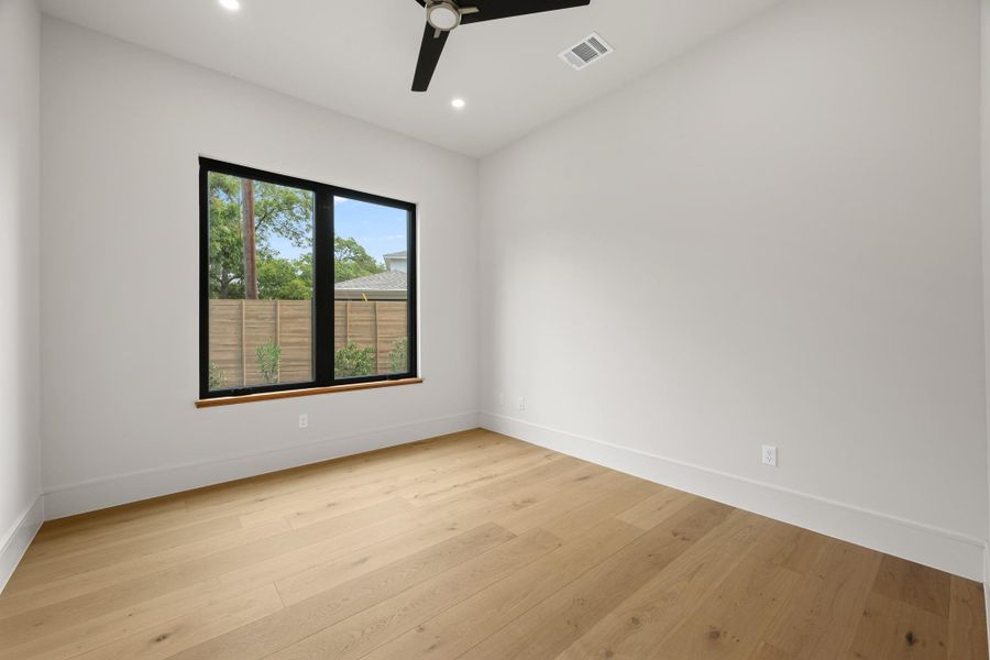 Rich hardwood flooring complements the clean lines of this modern bedroom with a large window.