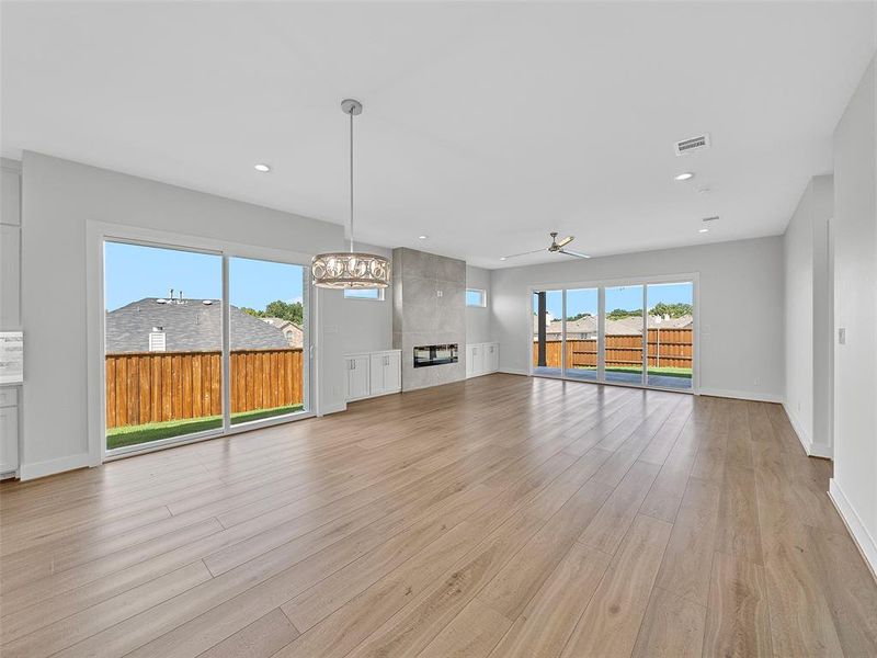 Unfurnished living room with light hardwood / wood-style floors, ceiling fan with notable chandelier, and a tiled fireplace