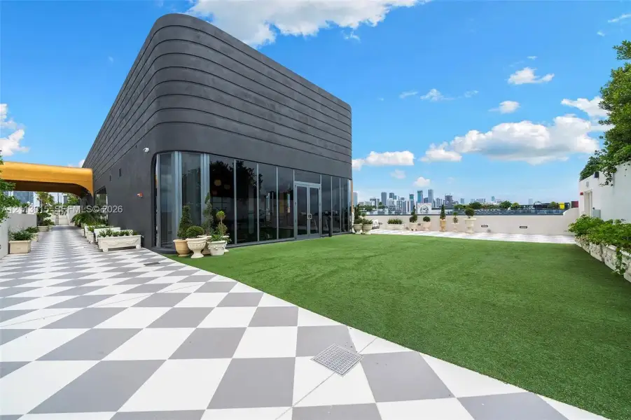 Rooftop terrace featuring large-format checkered paving, artificial turf surface, full-height glass window wall, and curved exterior structure