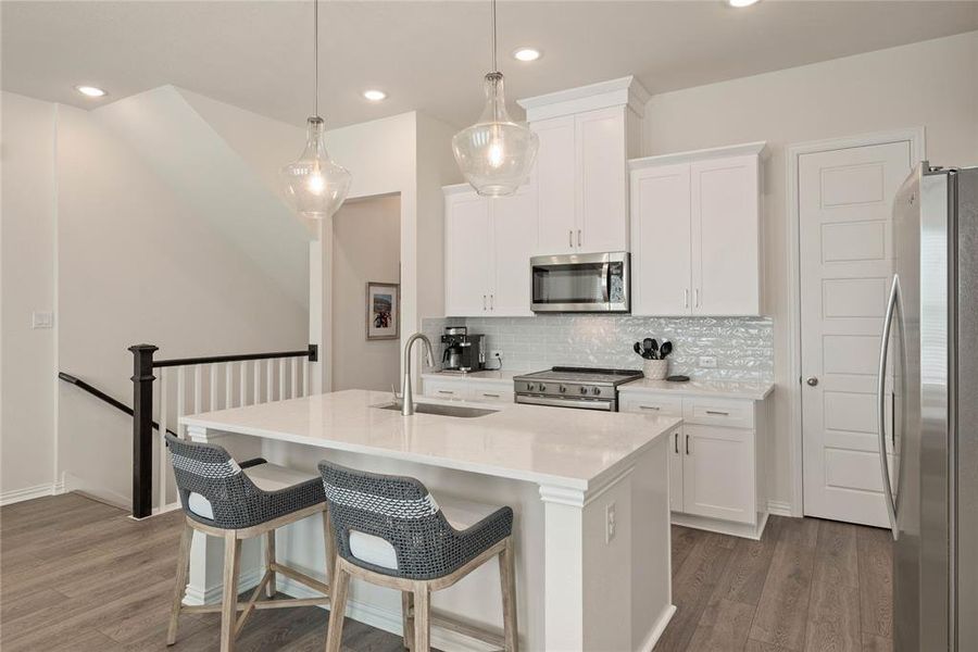 Kitchen with sink, white cabinetry, decorative light fixtures, appliances with stainless steel finishes, and a kitchen island with sink