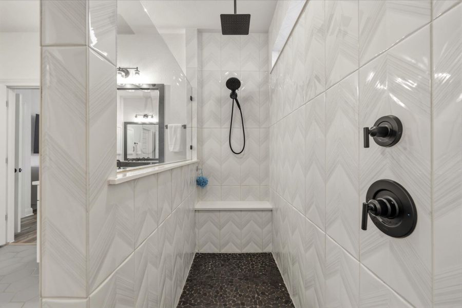 Contemporary shower featuring matte black fixtures, chevron-patterned wall tile, a built-in shower bench, and dark pebble-finish flooring